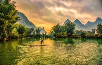 Man paddleboarding in lake against mountains during sunset