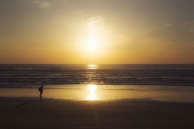 Scenic view of man walking on beach at sunset