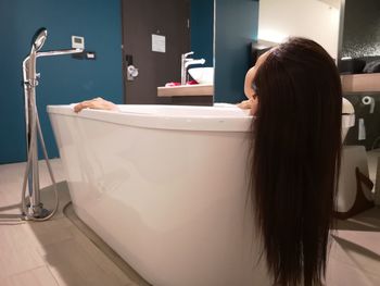 Woman with long hair lying in bathtub at home