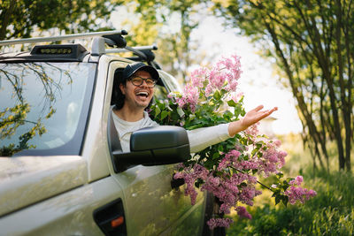 Hqppy smiling man with pink lilac flowers in car driving in forest