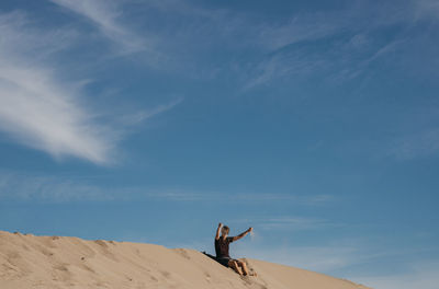Man with arms raised on sand against sky