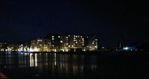 Illuminated buildings by river against sky at night