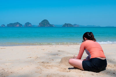 Rear view of man sitting on shore at beach against sky