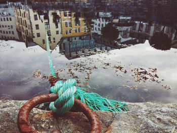 Rope tied on mooring ring with buildings reflecting in calm lake