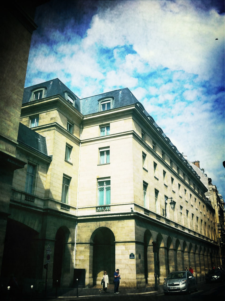 architecture, building exterior, built structure, sky, low angle view, car, transportation, land vehicle, cloud - sky, city, street, building, mode of transport, cloud, cloudy, road, window, street light, incidental people, city life