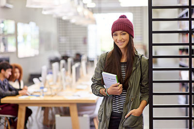 Smiling woman holding book standing with hand in pocket