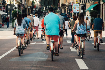 Rear view of people riding bicycles on road in city