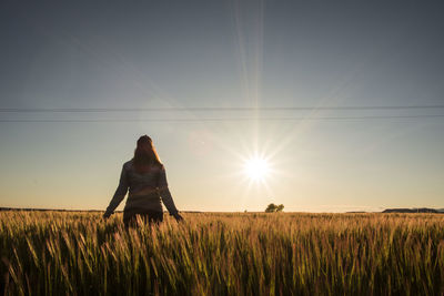 Rear view of woman standing on grassy field against sky