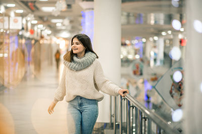 Smiling teenager girl standing by railing at shopping mall