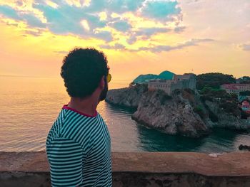 Side view of man looking at sea against sky during sunset 