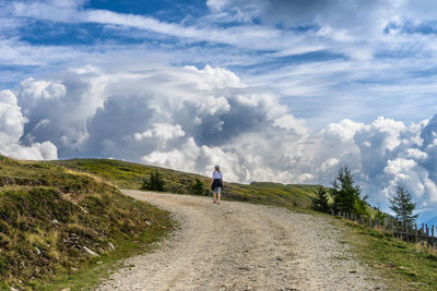 Rear view of man walking on road against sky