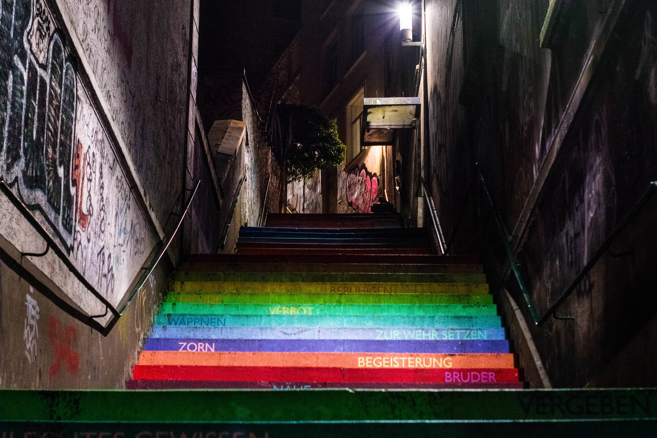 REAR VIEW OF MAN WALKING ON ILLUMINATED STAIRCASE OF BUILDING