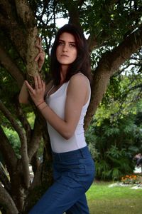 Portrait of beautiful young woman standing by tree trunk