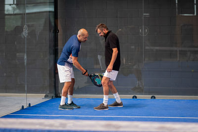 Monitor teaching padel class to man, his student - trainer teaches boy how to play padel on indoor 