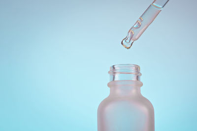 Face serum oil drop with dropper glass bottle pipette on blue background close up