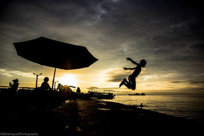 Silhouette people on beach against sky during sunset