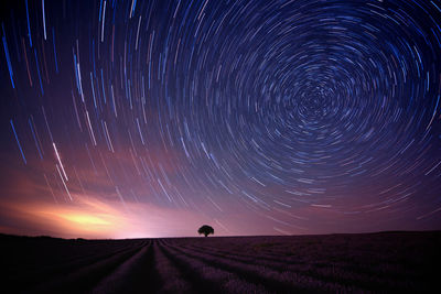Star trail over field against sky at night
