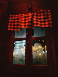 Illuminated light bulbs hanging from window of house at night