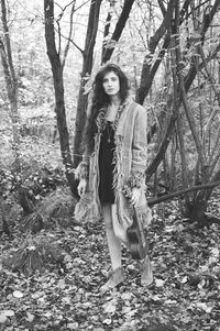 Portrait of young woman standing by tree trunk in forest