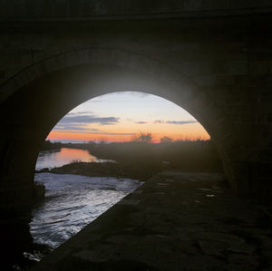 Arch bridge over river against sky during sunset