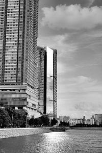 Modern buildings by river against sky in city