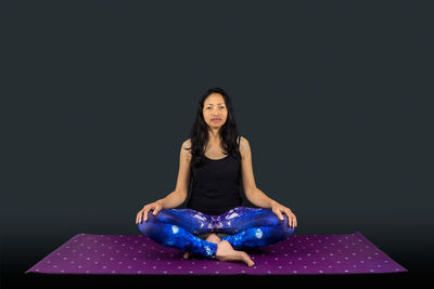 Portrait of woman sitting against black background