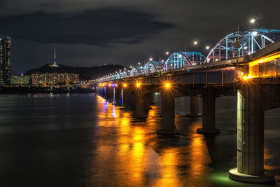 Illuminated bridge over sea against sky at night