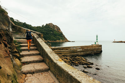 Rear view of man walking on pier over sea against sky