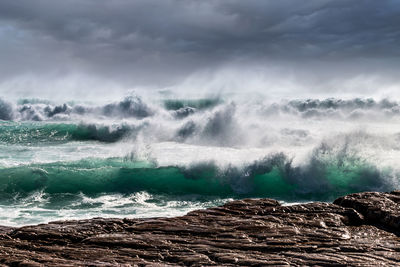 Waves splashing on rocks against sky