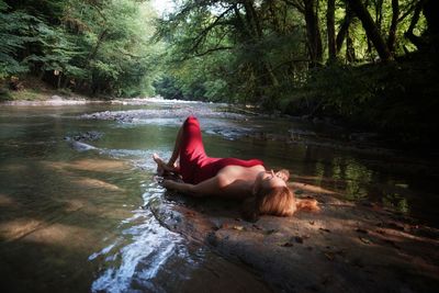 Woman sitting on riverbank in forest