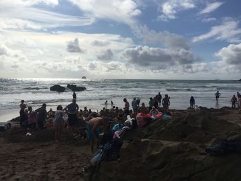 People at beach against cloudy sky