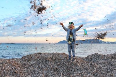 Full length of girl throwing leaves while standing on beach against sky