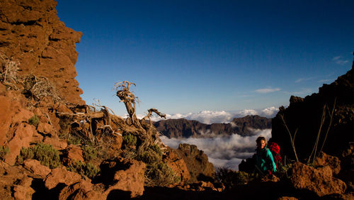 Woman sitting on mountain against sky