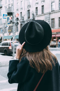 Rear view of woman holding hat while standing on street