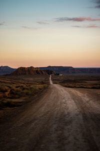 Dirt road leading towards against sky during sunset