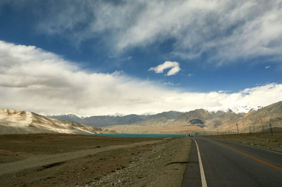 View of road along landscape against cloudy sky