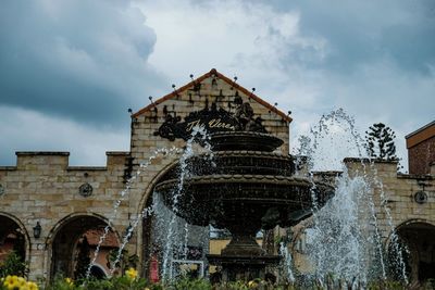 Low angle view of fountain by building against sky