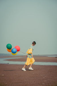 Full length of young woman holding colorful balloons at beach