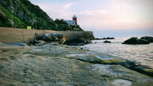 Lighthouse on rocks by sea against sky