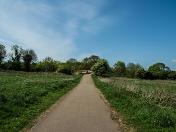 Empty road amidst field against sky