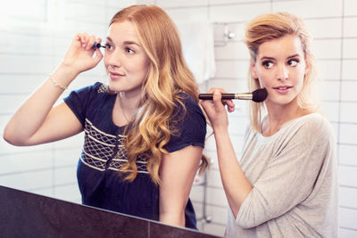 Young sisters applying makeup in mirror