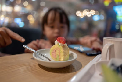 Cropped hand touching girl using smart phone with ice cream on table
