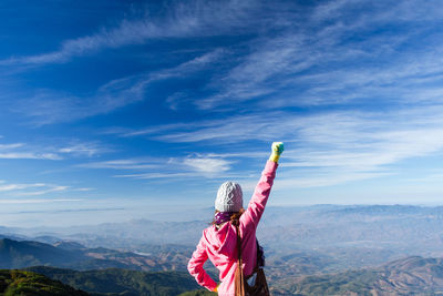Rear view of woman with arms outstretched standing against sky