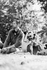 Man sitting by dog on grassy field