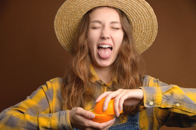 Attractive caucasian young woman in a plaid shirt and a straw hat with a cut orange fruit in her