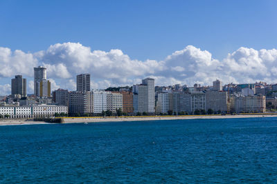 Sea by buildings against blue sky