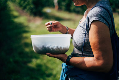 Side view of woman holding bowl with berries while standing on field