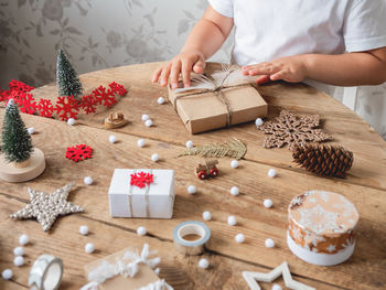 Child wrapped christmas presents in craft paper. wooden table with hand made new year gifts.