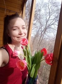 Young woman holding pink flowering plants by window