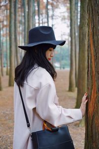 Side view of woman wearing hat standing against trees
